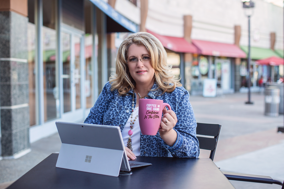 A woman sitting at an outdoor table with her laptop and coffee.