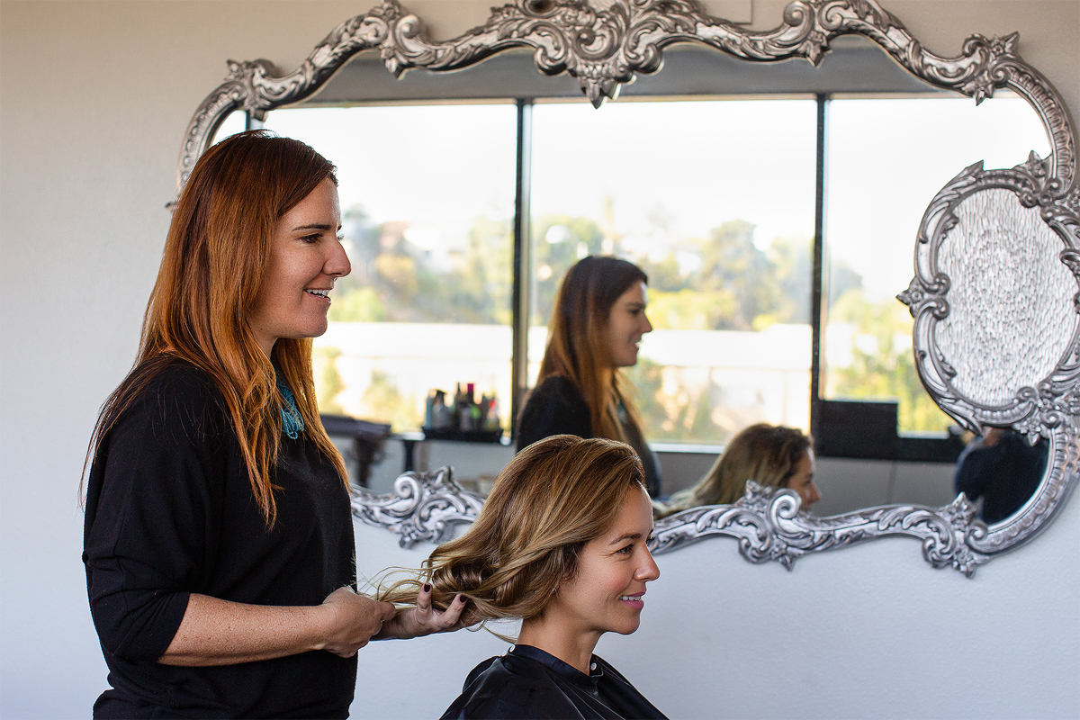 A woman getting her hair done in front of a mirror.