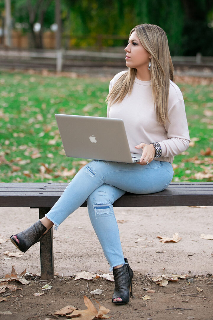 A woman sitting on top of a bench with a laptop.