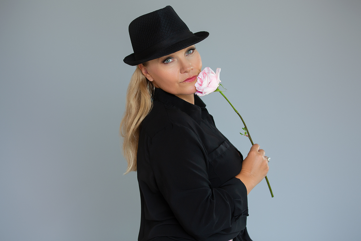 A woman in black shirt holding pink flower.