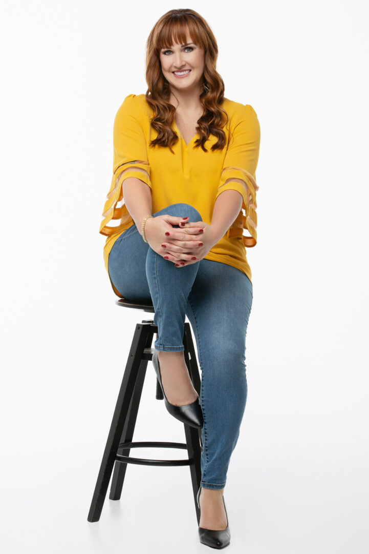 A woman sitting on top of a stool wearing jeans.